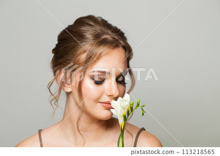 Pretty young adult woman with clean fresh skin smelling flower. Model with healthy skin close up 113218565
