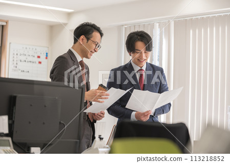 A male businessman in a suit having a meeting while holding documents 113218852