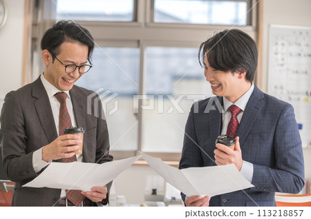 A male businessman in a suit having a meeting while holding documents 113218857