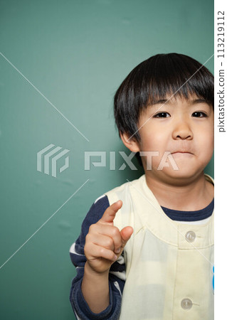 A 5-year-old nursery school child with a green background pointing up A 5-year-old nursery school child with a green background pointing up 113219112