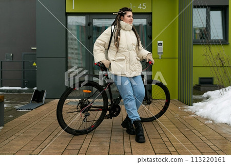 Woman Standing Next to Bike in Front of Building Woman Standing Next to Bike in Front of Building 113220161