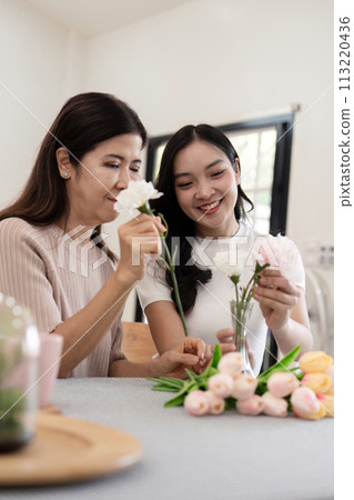 Senior mother and adult daughter happy on the table while arrange flowers in a vase together. Technology and lifestyle concept. Happy time together 113220436