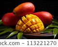 Mango is cut into cubes, surrounded by three whole mangos on the table with green leaves and black background 113221270