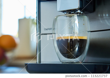 Fresh espresso in clear glass at morning. Coffee machine in kitchen, close up. Modern coffee maker with freshly brewed coffee in glass cup. Kitchen appliances Fresh espresso in clear glass at morning. Coffee machine in kitchen, close up. Modern coffee maker with freshly brewed coffee in glass cup. Kitchen appliances 113221737