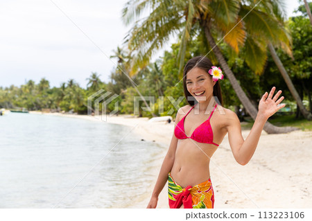 Luxury travel beach vacation woman in pareo waving hand saying hi hello on island, French Polynesia. Image is unretouched and model is without makeup. Authentic real people. Original Raw Image 113223106