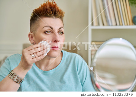 Middle-aged woman with a mirror taking care of her facial skin Middle-aged woman with a mirror taking care of her facial skin 113223379