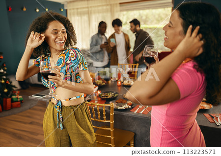 Cheerful young diverse female friends holding drinks and dancing at home kitchen during party time Cheerful young diverse female friends holding drinks and dancing at home kitchen during party time 113223571