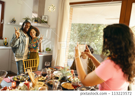 Woman making photo on phone for smiling friends couple during festive home party Woman making photo on phone for smiling friends couple during festive home party 113223572