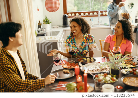 Happy friends enjoying in conversation and drinking wine during festive dinner at home party Happy friends enjoying in conversation and drinking wine during festive dinner at home party 113223574
