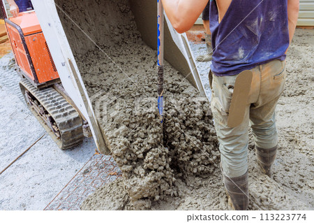 In construction of foundation, wet fresh cement is poured into framework in ground from concrete buggy In construction of foundation, wet fresh cement is poured into framework in ground from concrete buggy 113223774