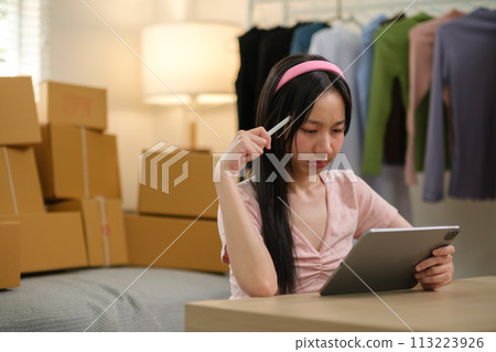 Asian business woman on sofa using a tablet checking customer order online shipping boxes at home. Starting SME Small business entrepreneur freelance. Online business, SME Work home concept. 113223926
