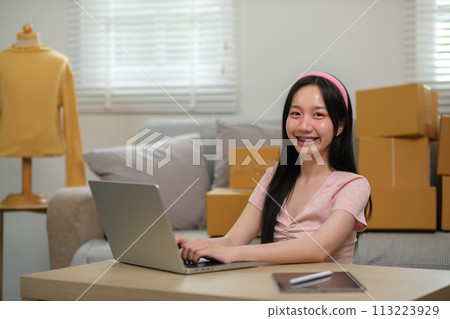 Asian business woman on sofa using a laptop checking customer order online shipping boxes at home. Starting SME Small business entrepreneur freelance. Online business, SME Work home concept. Asian business woman on sofa using a laptop checking customer order online shipping boxes at home. Starting SME Small business entrepreneur freelance. Online business, SME Work home concept. 113223929