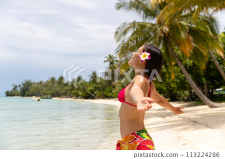 Happy free summer vacation beach bikini body woman enjoying sun carefree with open arms sunbathing at paradise beach in skirt and flower. Image is unretouched and model without makeup. Raw Image 113224286