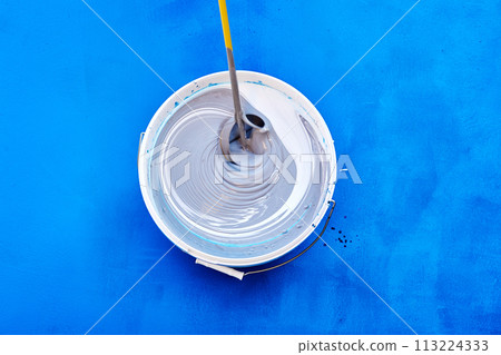 Top view captures process of stirring rod mixing fresh, white paint in bucket. Top view captures process of stirring rod mixing fresh, white paint in bucket. 113224333