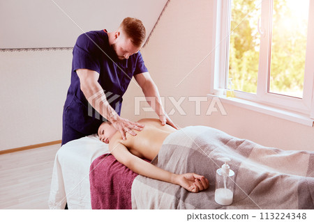 Young masseur brought massage table to home woman in her 20s to give her back massage. 113224348