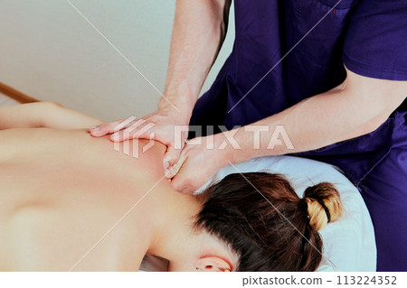 White woman receives physiotherapy treatments lying face down on massage table, European female in her 20s, at masseuse appointment. 113224352