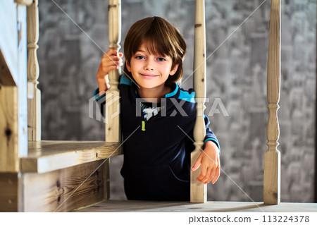 Little Caucasian boy smiles while looking through balusters of wooden staircase railing in his home. Little Caucasian boy smiles while looking through balusters of wooden staircase railing in his home. 113224378
