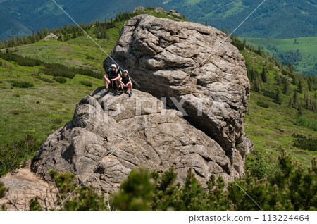 Dad and son are sitting on a big stone in the mountains, Vukhatiy Kamin mountain in the Carpathians of Ukraine. Dad and son are sitting on a big stone in the mountains, Vukhatiy Kamin mountain in the Carpathians of Ukraine. 113224464