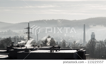 Smoke rises from chimneys against a backdrop of hazy hills, as smog blankets an industrial town at dawn, highlighting environmental concerns. 113225557