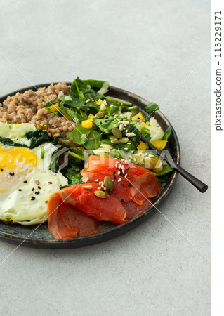 Buckwheat with fried egg and salmon fish, mix salad with fresh herbs and peppers Buckwheat with fried egg and salmon fish, mix salad with fresh herbs and peppers 113229171