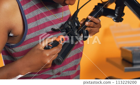 Woman uses screwdriver to make sure brake levers are secure on handlebars in studio background atelier shop. Close up shot of expert mechanic unscrewing bike parts in order to mend them 113229200