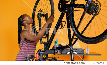 Engineer doing bike servicing in studio background repair shop, replacing defective wheel. Professional fixing busted bicycle tires and mending damaged rear derailleur, camera B 113229251