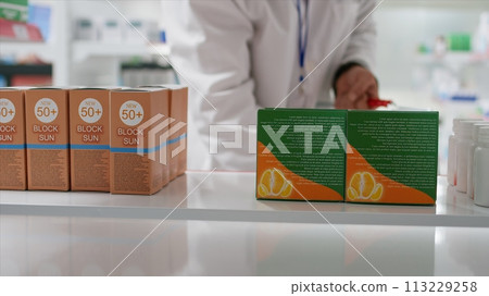 POV of druggist taking nutritional vitamins boxes from shelves, replacing them with other medication. Employee rearranging pharmaceutical products in healthcare facility. Tripod shot. POV of druggist taking nutritional vitamins boxes from shelves, replacing them with other medication. Employee rearranging pharmaceutical products in healthcare facility. Tripod shot. 113229258