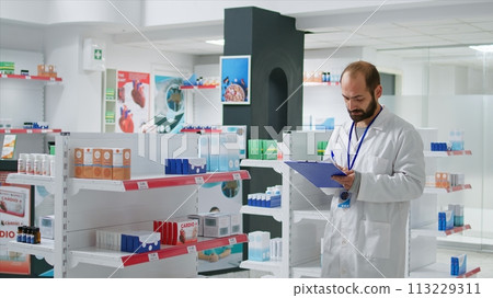Pharmacy worker writing every medical product on inventory, creating long list with all pharmaceutics and medicaments in drugstore. Pharmacist ensuring variety of healthcare supplies. Camera 1. 113229311