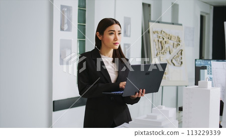 Design specialist reviewing measurements on 3d maquette model, working on remodeling property for a customer. Expert engineer looking at floor plans and architectural sketches on laptop. 113229339