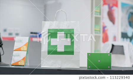 Empty pharmacy with pills and vitamins at cash register, paper bag containing pharmaceuticals alongside greenscreen layer on pill box at checkout area. Chromakey copyspace design next to purchase. 113229340