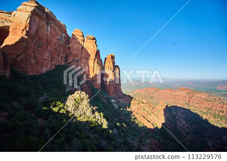 Majestic Red Rock Spires of Sedona with Greenery Against Blue Sky 113229576