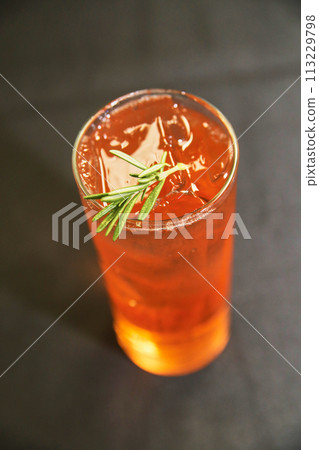 Chilled Amber Beverage with Rosemary Garnish Close-Up 113229798