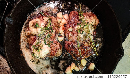Sizzling Steaks in Cast Iron Skillet with Herbs and Garlic, Top View Sizzling Steaks in Cast Iron Skillet with Herbs and Garlic, Top View 113229957