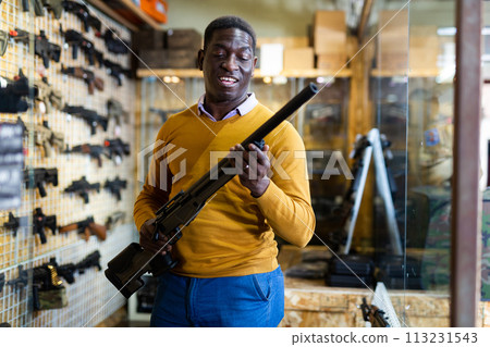 African american man chooses pump-action shotgun in gun store closeup African american man chooses pump-action shotgun in gun store closeup 113231543