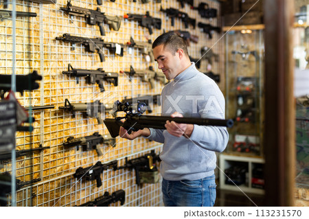 Adult man chooses rifle with telescopic sight and silencer Adult man chooses rifle with telescopic sight and silencer 113231570