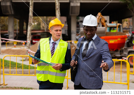 Engineer and architect are discussing options for laying a pipe on street 113231571