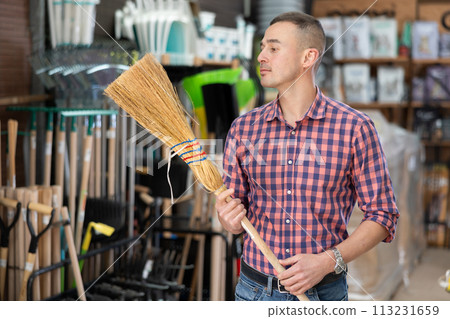 Male buyer carefully chooses broom in hardware store to clean yard of her house Male buyer carefully chooses broom in hardware store to clean yard of her house 113231659