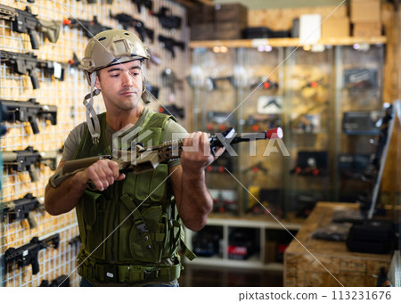 Male in military shop choosing shotgun in store with rifle equipment Male in military shop choosing shotgun in store with rifle equipment 113231676