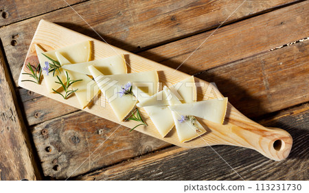 Delicious cheese slices served with rosemary sprouts and flowers on wooden cutting board 113231730