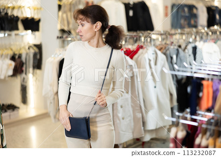 Middle-aged woman watching excitedly large stock of clothes in clothing store Middle-aged woman watching excitedly large stock of clothes in clothing store 113232087
