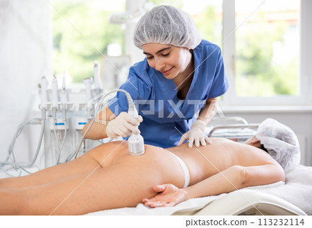 Female cosmetologist performing procedure using cooling attachment on woman client buttocks Female cosmetologist performing procedure using cooling attachment on woman client buttocks 113232114