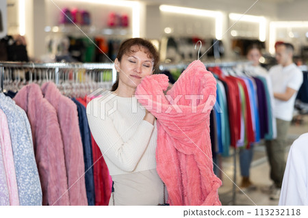 Middle-aged woman choosing convenient bathrobe in clothing store Middle-aged woman choosing convenient bathrobe in clothing store 113232118