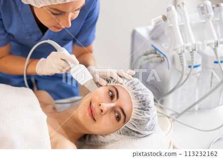 Young female patient undergoing facial skin cleansing with ultrasonic shovel 113232162