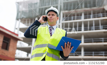 Young engineer, controlling the progress of work on a laptop, talking on a mobile phone Young engineer, controlling the progress of work on a laptop, talking on a mobile phone 113232280