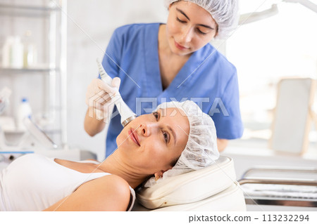 Female client undergoing anti-aging ultrasonic phonophoresis procedure on face 113232294