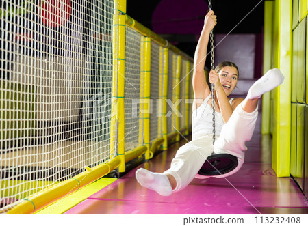 Cheerful girl swinging on indoor zip line at play center 113232408