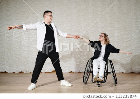 Long shot of young Caucasian man and woman with disability in wheelchair performing dance on stage, copy space 113235874