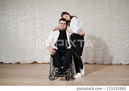 Long shot of young Caucasian woman and mature man with disability in wheelchair having performance on stage, copy space 113235880