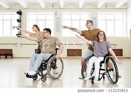 Group of four cheerful diverse people practicing modern dance with wheelchairs in spacious hall Group of four cheerful diverse people practicing modern dance with wheelchairs in spacious hall 113235913