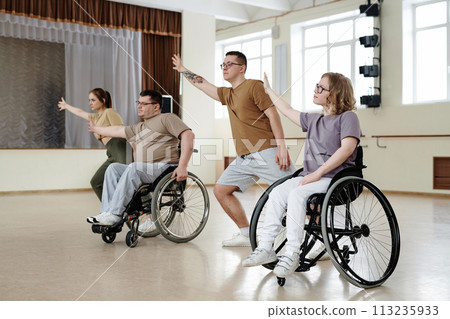 Group of man and woman in wheelchairs and their partners practicing dance with wheelchairs in studio, long shot Group of man and woman in wheelchairs and their partners practicing dance with wheelchairs in studio, long shot 113235933